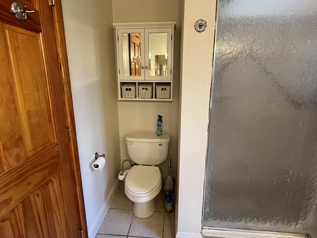 bathroom featuring toilet, a stall shower, baseboards, and tile patterned flooring