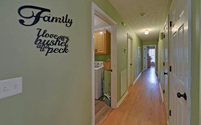 corridor featuring a textured ceiling, washer and clothes dryer, and light hardwood / wood-style floors