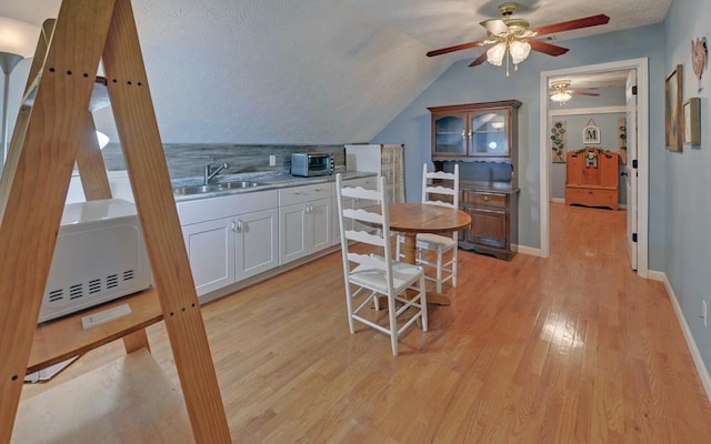 kitchen featuring white cabinetry, lofted ceiling, sink, backsplash, and light wood-type flooring