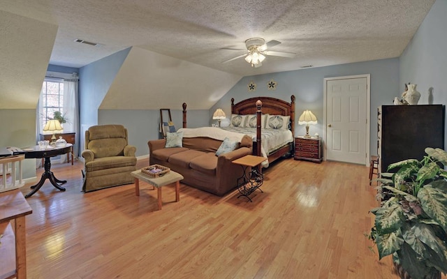 bedroom with ceiling fan, vaulted ceiling, a textured ceiling, and light hardwood / wood-style floors