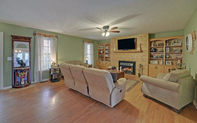 living room featuring built in features, a fireplace, light hardwood / wood-style floors, and a textured ceiling