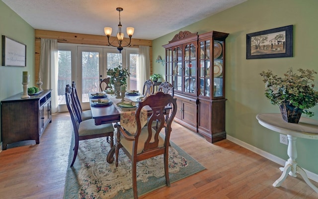 dining space with an inviting chandelier, a textured ceiling, light wood-type flooring, and french doors