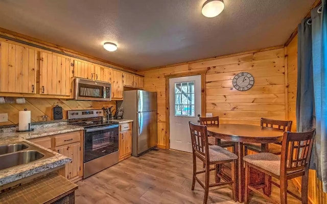 kitchen featuring wood walls, light brown cabinetry, light hardwood / wood-style floors, and appliances with stainless steel finishes