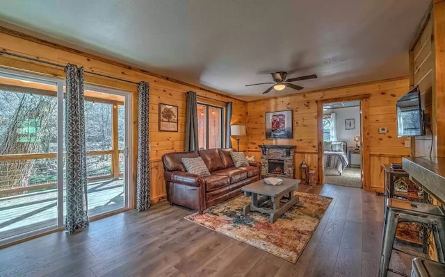 living room with a stone fireplace, wood walls, ceiling fan, and dark hardwood / wood-style floors