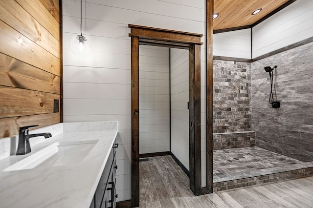 bathroom featuring vanity, a tile shower, and wood walls