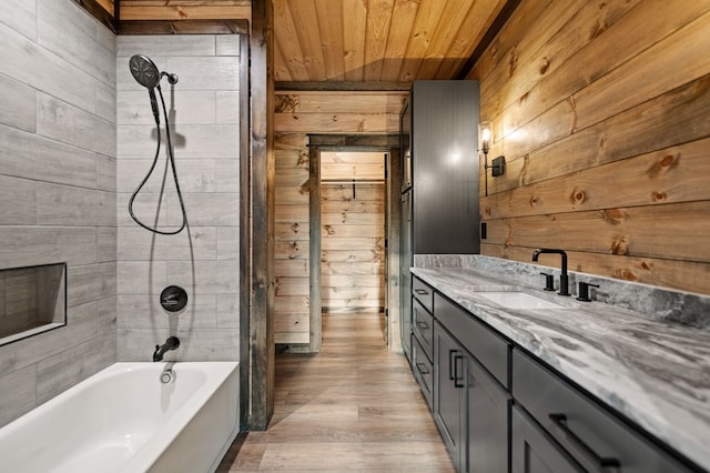 bathroom with hardwood / wood-style floors, wood walls, tiled shower / bath combo, vanity, and wooden ceiling