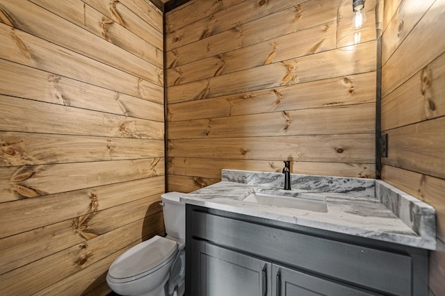 bathroom with toilet, vanity, and wooden walls