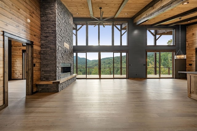 unfurnished living room featuring a stone fireplace, beamed ceiling, wood-type flooring, a high ceiling, and wood ceiling