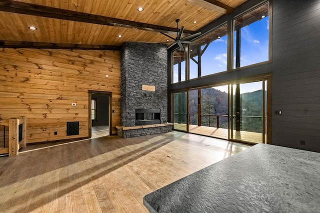 unfurnished living room with hardwood / wood-style floors, a stone fireplace, high vaulted ceiling, and beam ceiling