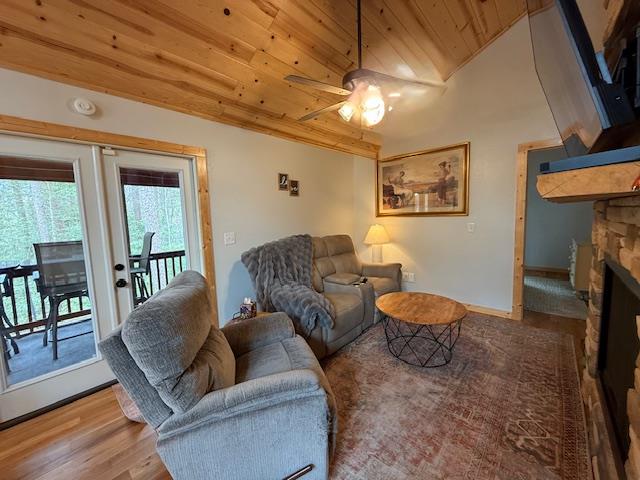 living room with a stone fireplace, wooden ceiling, wood finished floors, baseboards, and vaulted ceiling