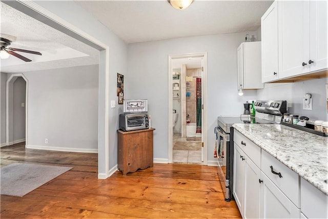 kitchen featuring light stone counters, ceiling fan, electric range, white cabinetry, and light hardwood / wood-style flooring