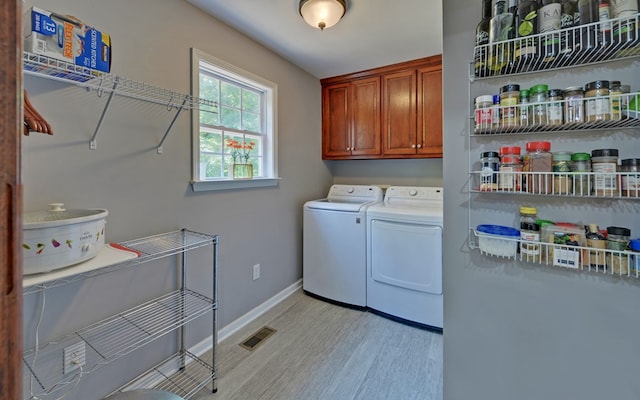 clothes washing area with cabinets, washing machine and dryer, and light wood-type flooring