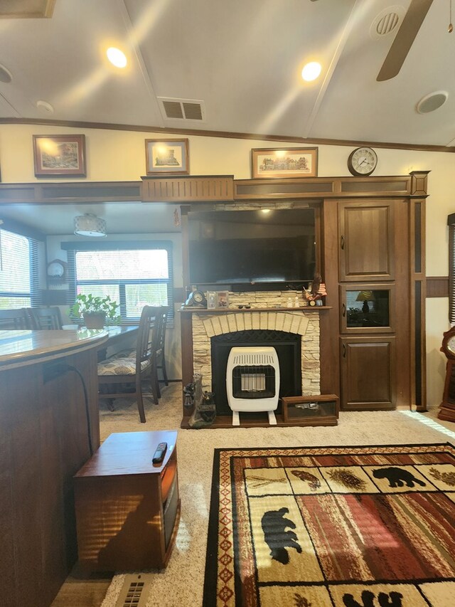 carpeted living room featuring crown molding, visible vents, ceiling fan, and a stone fireplace