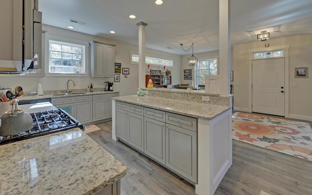 kitchen with pendant lighting, light hardwood / wood-style flooring, light stone counters, and sink