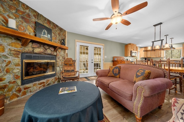 living room with a stone fireplace, french doors, ceiling fan, and wood finished floors