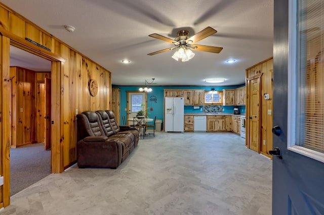 living room featuring ceiling fan with notable chandelier, light colored carpet, and wood walls