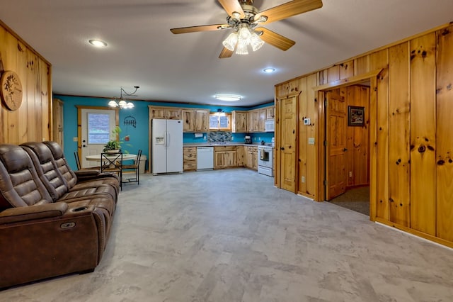 living room with ceiling fan with notable chandelier and wooden walls