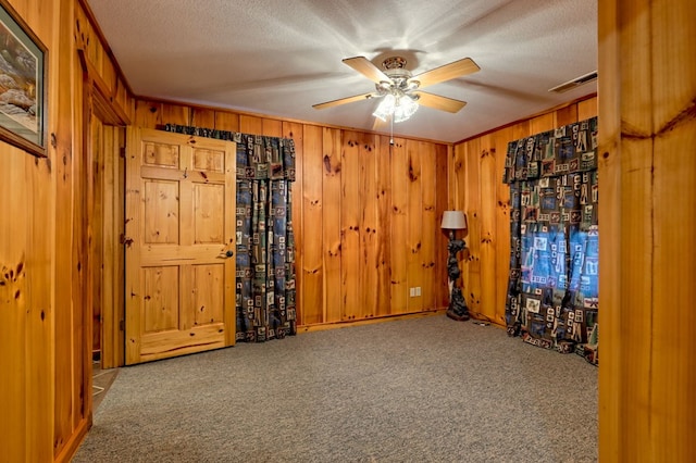 empty room with carpet flooring, a textured ceiling, ceiling fan, and wood walls