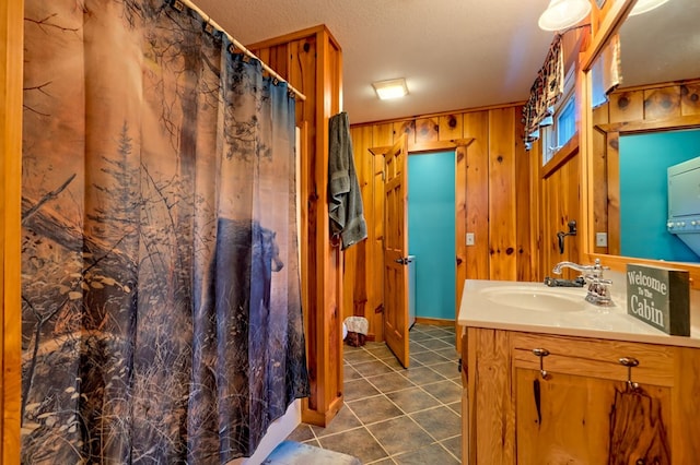 bathroom with a textured ceiling, vanity, and wood walls