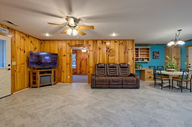 living room featuring wood walls and ceiling fan with notable chandelier