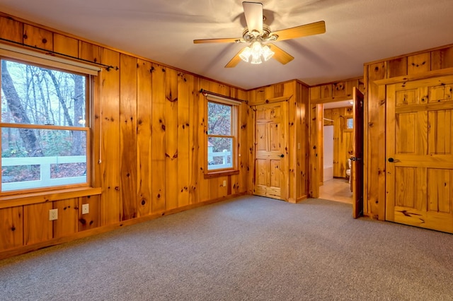 interior space with ceiling fan, light colored carpet, wooden walls, and multiple windows