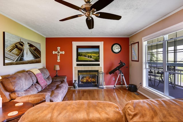 living area with light wood-type flooring, ornamental molding, a textured ceiling, and a tile fireplace