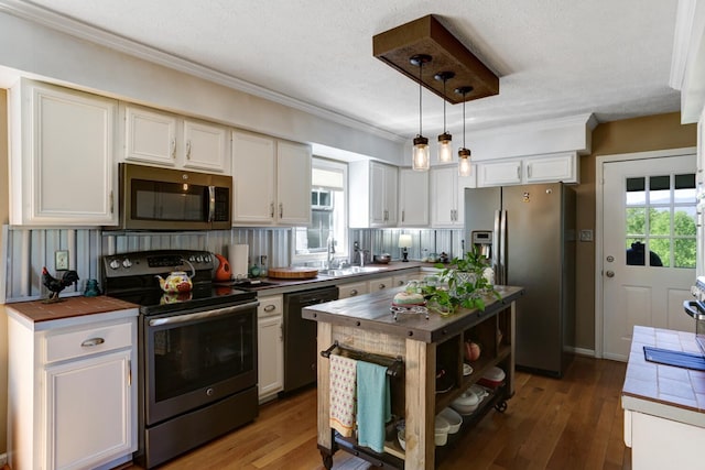 kitchen featuring white cabinets, tile countertops, appliances with stainless steel finishes, decorative light fixtures, and a sink