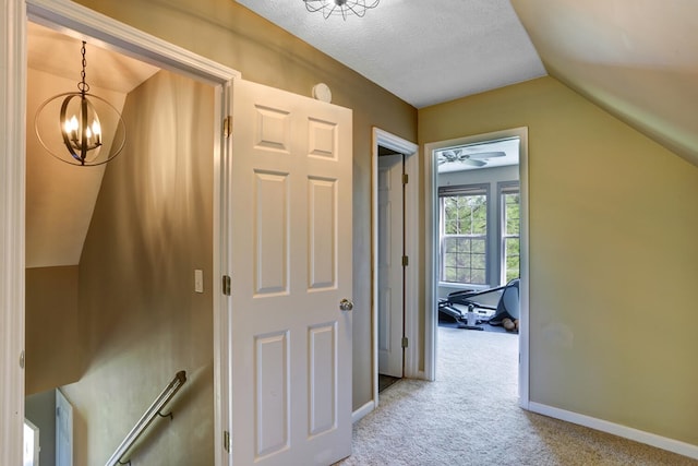 corridor featuring a notable chandelier, lofted ceiling, light carpet, a textured ceiling, and baseboards