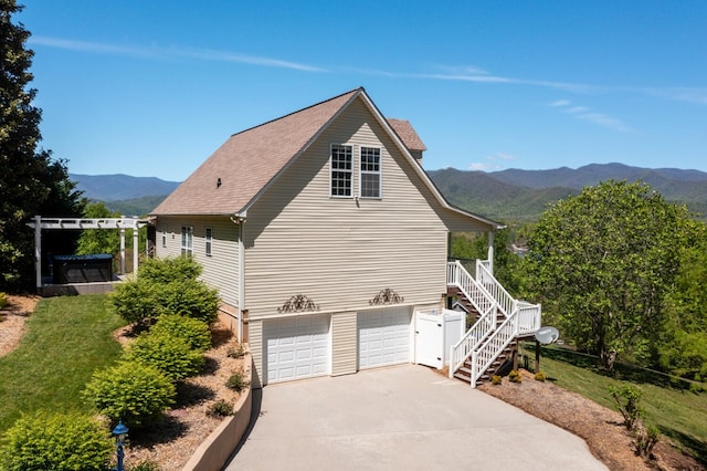 view of home's exterior with driveway, an attached garage, stairs, a yard, and a mountain view