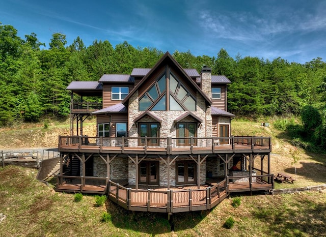 rear view of house with a deck, metal roof, stone siding, french doors, and a chimney