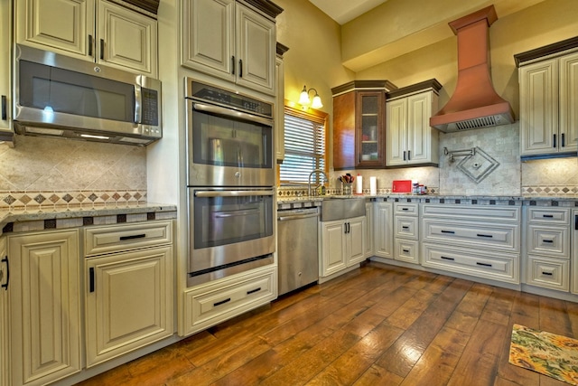 kitchen with stainless steel appliances, decorative backsplash, dark wood finished floors, glass insert cabinets, and custom range hood