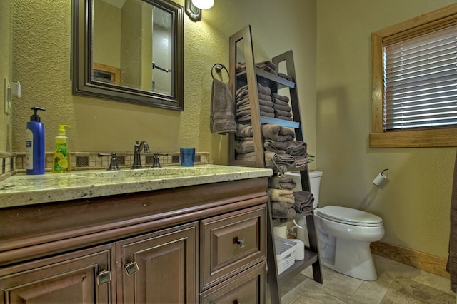 bathroom with a textured wall, toilet, vanity, baseboards, and tile patterned floors