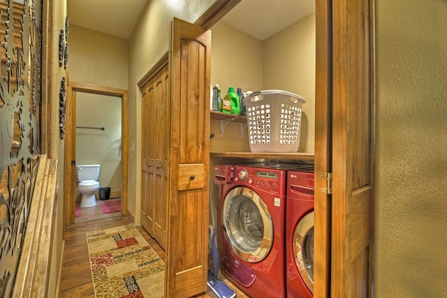 clothes washing area featuring a textured wall, laundry area, washer and clothes dryer, and wood finished floors