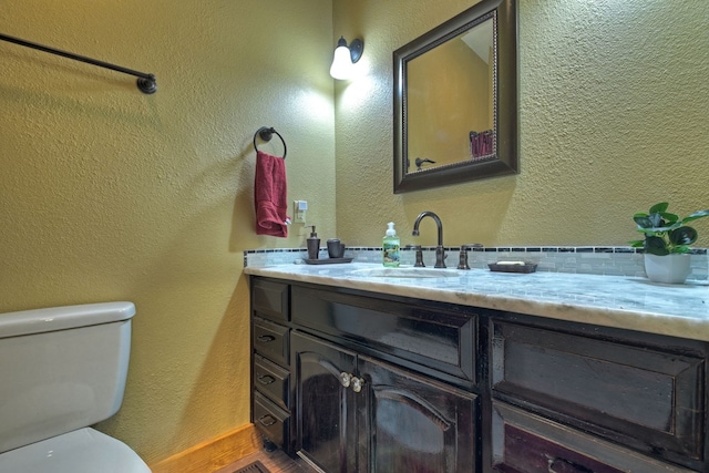 half bath with a textured wall, vanity, toilet, and wood finished floors