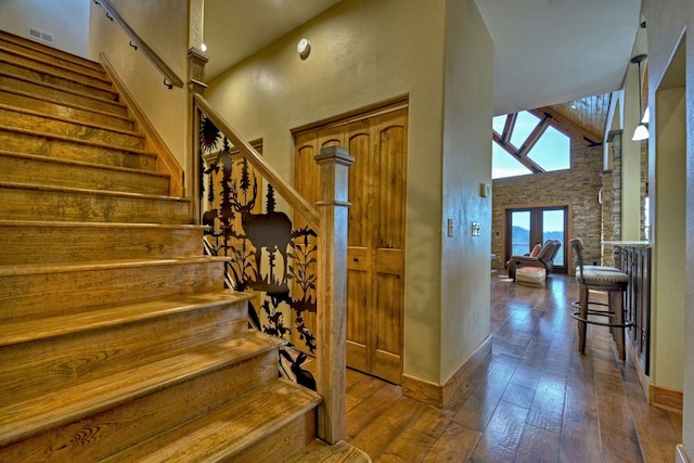 stairs with a textured wall, a high ceiling, visible vents, baseboards, and hardwood / wood-style floors