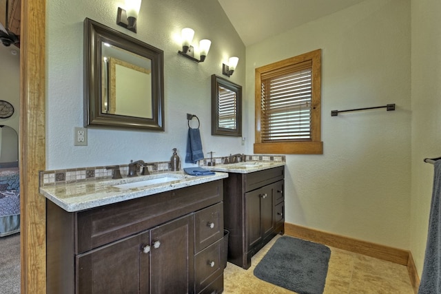 full bath featuring two vanities, a sink, connected bathroom, and baseboards