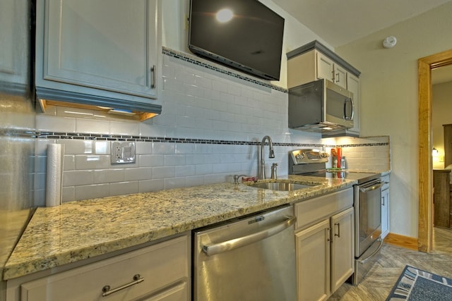 kitchen featuring baseboards, decorative backsplash, appliances with stainless steel finishes, light stone counters, and a sink