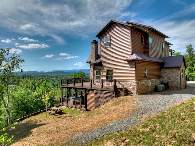 view of home's exterior featuring metal roof, a deck with mountain view, central AC, stone siding, and faux log siding