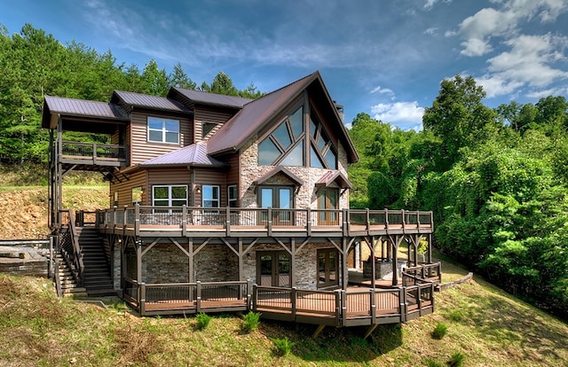 rear view of house with french doors, metal roof, stone siding, faux log siding, and a wooden deck