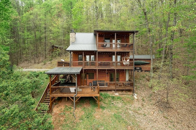 rear view of property with a chimney, faux log siding, and a view of trees