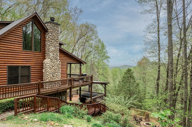 view of home's exterior featuring a chimney, log veneer siding, a view of trees, and a wooden deck