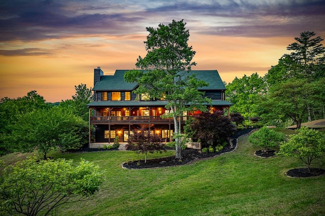 back of house at dusk featuring a chimney, a lawn, and a deck