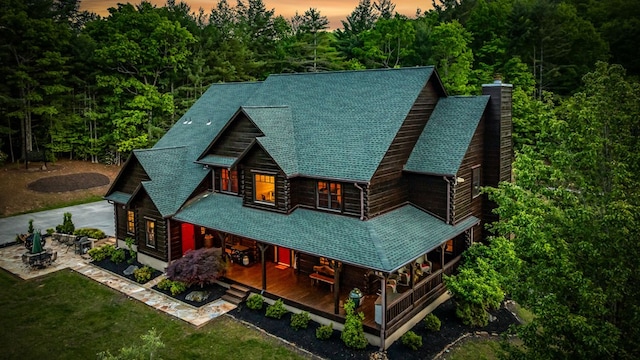 back of property featuring driveway, a chimney, a yard, covered porch, and a view of trees