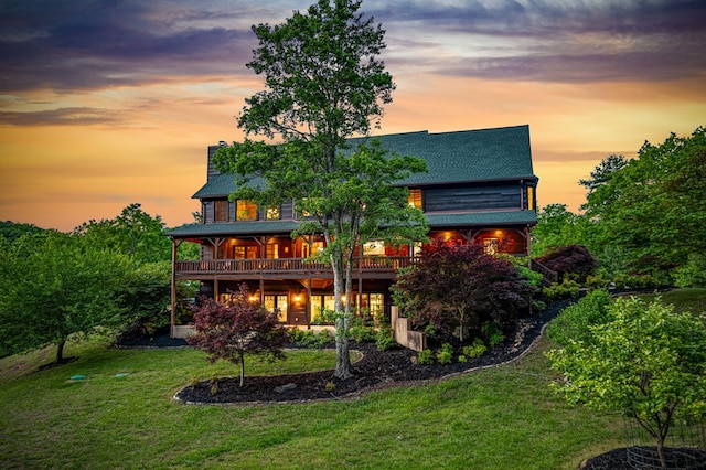 back of house at dusk featuring a lawn, a chimney, roof with shingles, and a deck