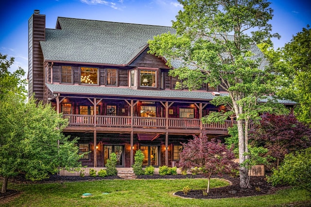 rear view of property featuring a chimney, a yard, a shingled roof, and a deck