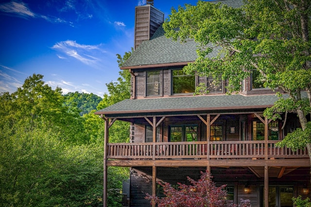 rear view of property with a shingled roof, a chimney, and a wooden deck