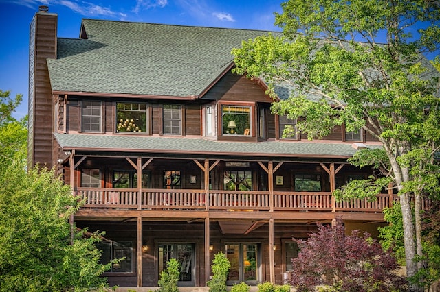 rear view of house featuring a chimney, roof with shingles, and a deck