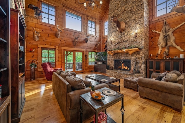 living room with high vaulted ceiling, plenty of natural light, hardwood / wood-style floors, wooden walls, and a stone fireplace