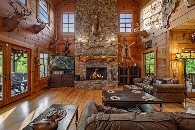 living room with high vaulted ceiling, wood walls, healthy amount of natural light, hardwood / wood-style floors, and a stone fireplace