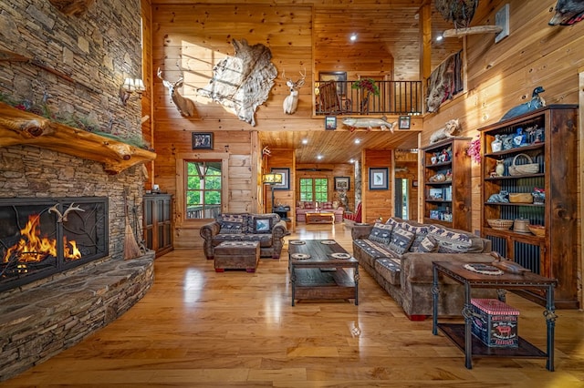 living room with a high ceiling, wooden walls, hardwood / wood-style flooring, and a stone fireplace